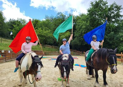 Drei Reiterinnen auf drei Pferden reiten nebeneinander auf einem Sandplatz und schwenken jeweils eine große Fahne