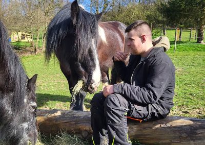 Ein Mann sitzt im Freien auf einem liegenden Baumstamm und blickt nachdenklich zur Seite.