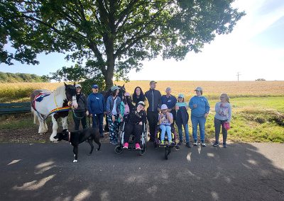 Eine Gruppe von etwa zwölf Personen, darunter einige in Rollstühlen, steht unter einem Baum