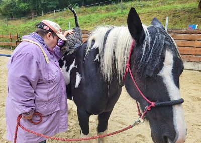 Eine Person in einer lilafarbenen Jacke steht neben einem schwarz-weißen Pferd